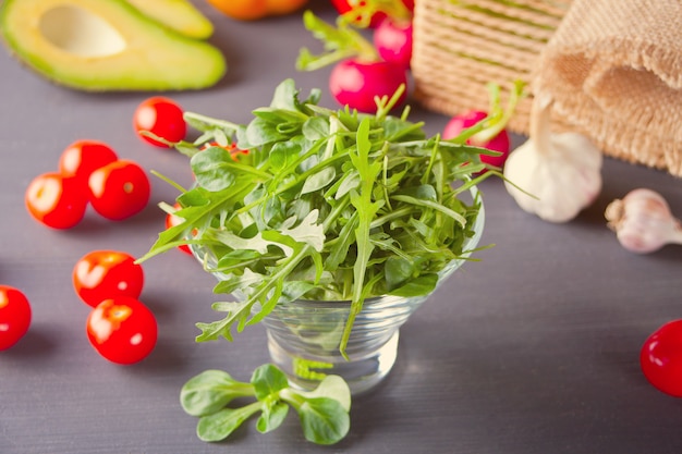 Wet fresh arugula in a bowl with vegetables on the background.