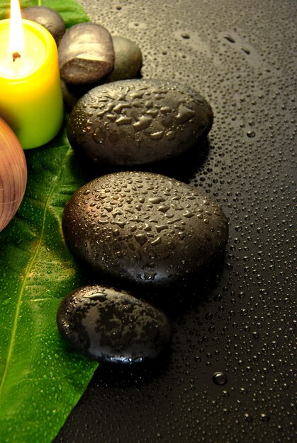 Wet massage stones with green leaf and water drops