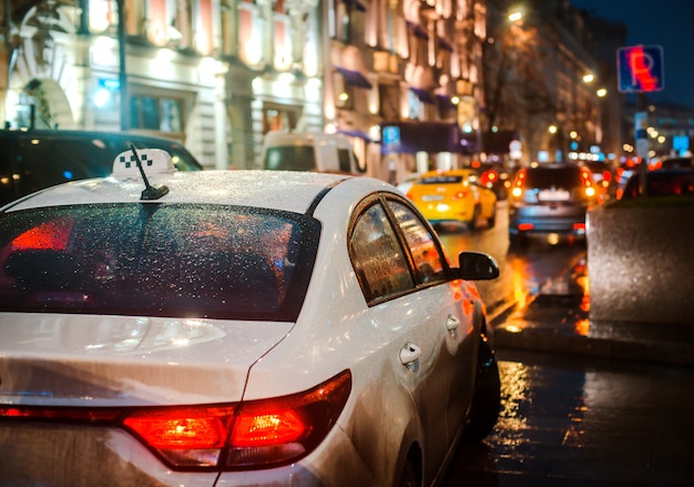 Automobile del marciapiede delle pozze delle luci variopinte luminose di riflessione del bokeh della pioggia della via della città di notte bagnata