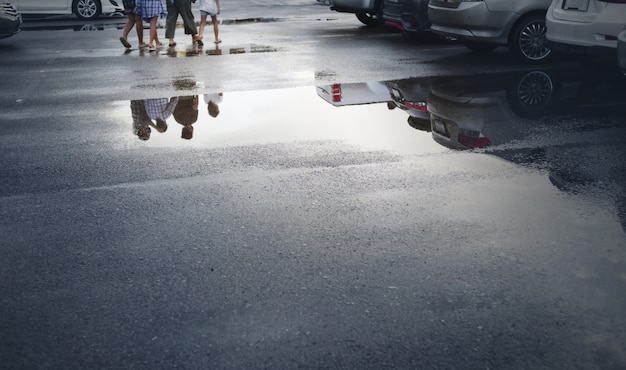 激しい雨が降った後の濡れた駐車スペースは、車の反射と地面の水たまりに人を歩いています。選択的な焦点。