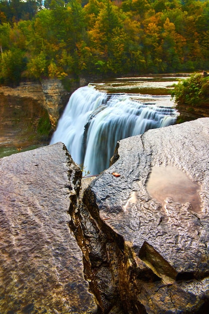 Wet rock wall with puddle and crack in foreground by huge waterfall pouring over cliffs into fall ca