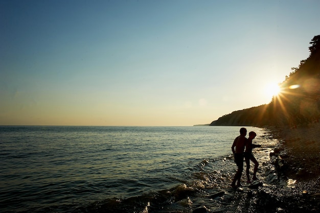 人々の波の夕日のシルエットに洗われた濡れた海の岩