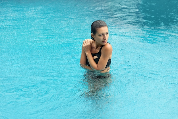 Wet sexy blackhair woman in swimsuit posing at pool.