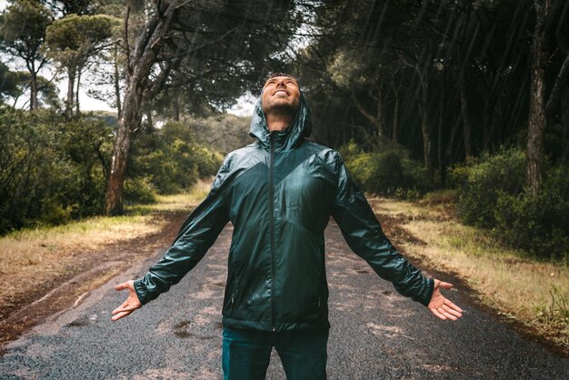 雨を楽しんでいるフード付きのびしょ濡れのジャケットの濡れた笑顔の男レインコートの男は大雨の中に立っていた