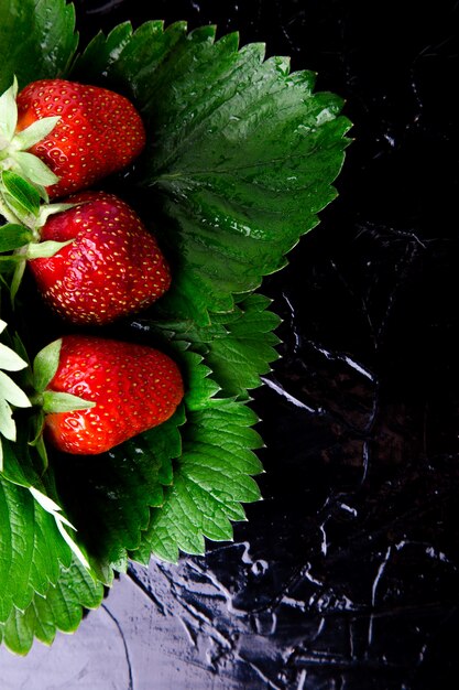 Wet strawberry with leaves on black.