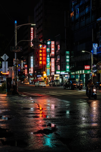 Wet street by illuminated buildings in city during rainy season at night