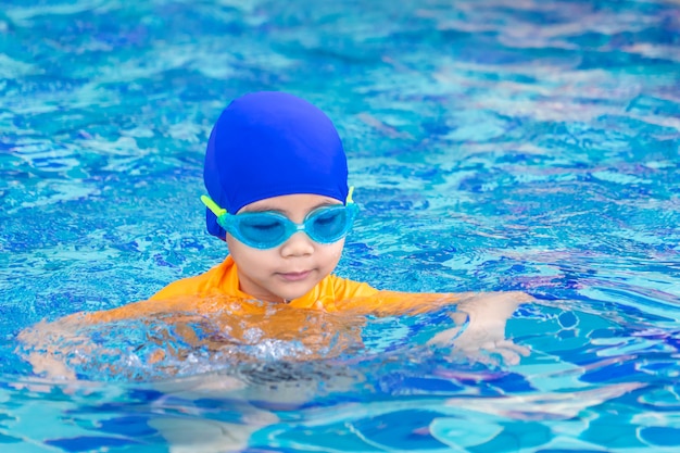 水泳のスーツを持つウェットスーツのアジアの男の子は、プールで泳いでいます