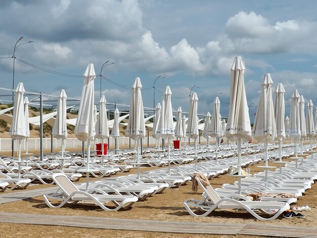 Wet sunbeds and umbrellas on the sea beach during heavy rain storm Rolled up parasol on the beach against dark cloudy sky Invasion of a typhoon cyclone or storm on the sea or ocean Beach season