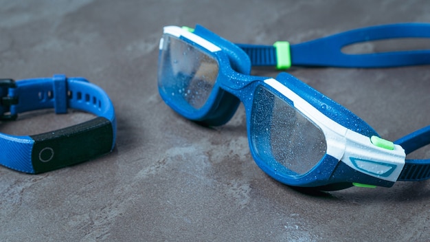 Wet swimming goggles and fitness bracelet on a stone surface