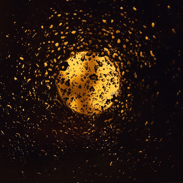 wet window glass with lots of rain drops and view of the night  sky with the gold glowing moon. 