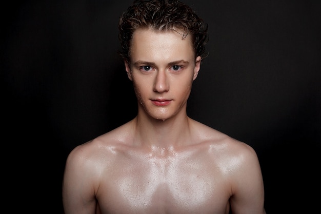 Wet young man with black hair on a black background