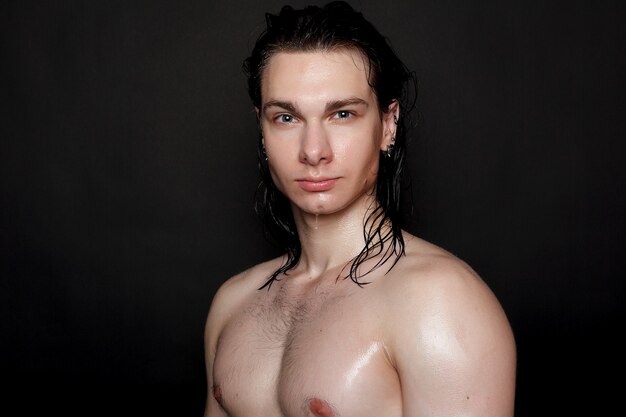 Wet young man with black hair on a black background