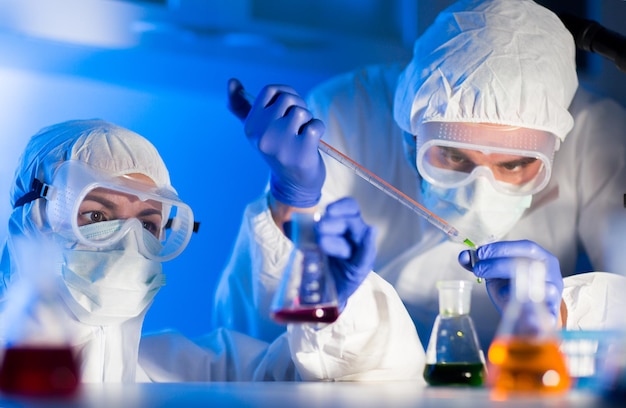 wetenschap, scheikunde, biologie, geneeskunde en mensen concept - close-up van jonge wetenschappers met pipet en kolven die test of onderzoek maken in klinisch laboratorium