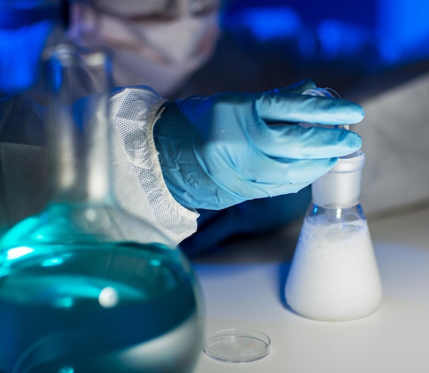 wetenschap, scheikunde, biologie, geneeskunde en mensen concept - close-up van wetenschapper met het gieten van chemisch poeder in de kolf en het maken van test of onderzoek in klinisch laboratorium