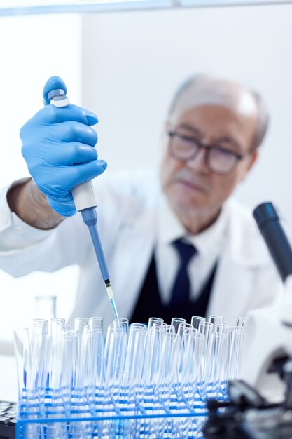 Wetenschapper met beschermingsuitrusting met behulp van druppelpipet-engineering vaccinbehandeling. Senior professionele chemicus die pippete met blauwe oplossing gebruikt voor microbiologische tests.