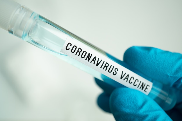 Wetenschapper met reageerbuis met covid-19 of coronavirus vaccinetiket, laboratoriumtests voor het uitvinden van pandemische medicatie