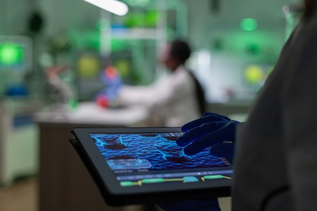 Foto wetenschapper-onderzoeker arts die genetische mutatietest analyseert met behulp van tablet terwijl haar collega biologische expertise typt op de computer op de achtergrond