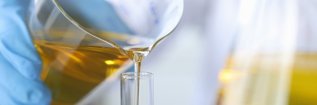 Wetenschapper scheikundige olie uit de kolf gieten in glas close-up kwaliteitscontrole van eetbare oliën