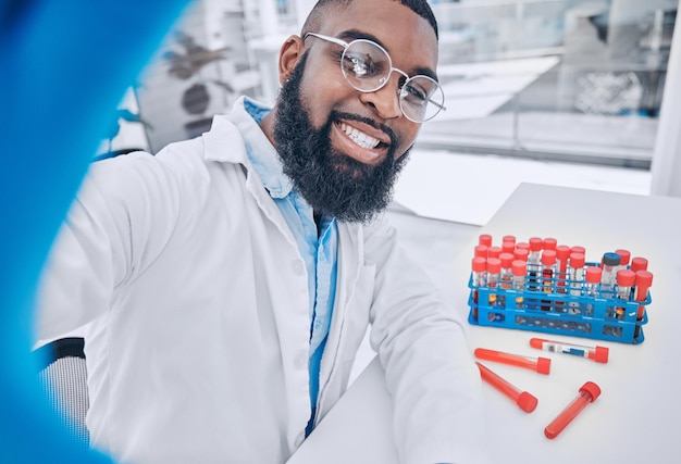 Wetenschapper selfie en man met bloedonderzoek en blij van medisch en gezondheidszorgwerk Afrikaanse mannelijke arts portret en profielfoto voor sociale media en chemietest in een wetenschappelijk laboratorium