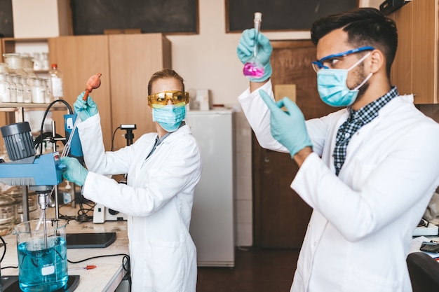 Wetenschappers en onderzoekers van middelbare leeftijd met gezichtsbeschermende maskers werken in een chemisch laboratorium aan het coronavirusvaccin.