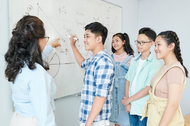 Wetenschapsleraar stelling uit te leggen aan groep studenten en schooljongen te vragen om vergelijking op het whiteboard te schrijven