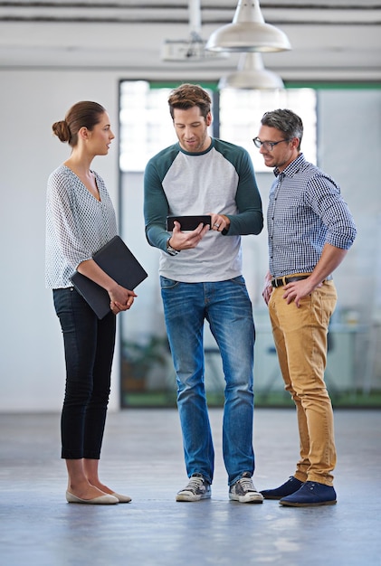 Weve got the information we need at our fingertips Three creative colleagues discussing information on a digital tablet in an open office space