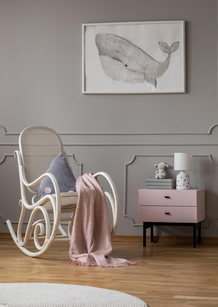 Photo whale on poster in fashionable baby room with white rocking chair and pastel pink nightstand with books and lamp