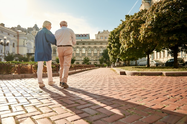 What a beautiful day back view of elderly stylish couple walking together outdoors