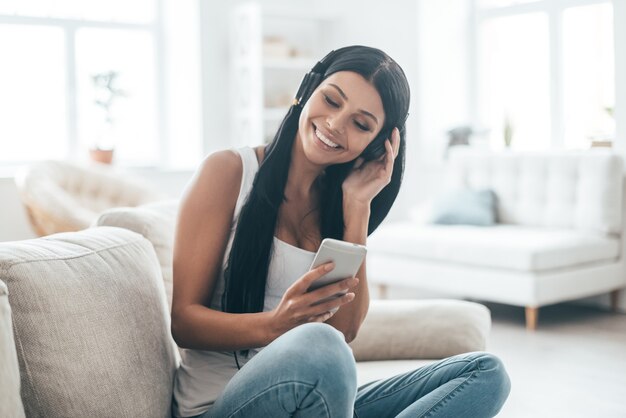 What a cool song! Attractive young woman listening music and smiling while sitting on the couch at home