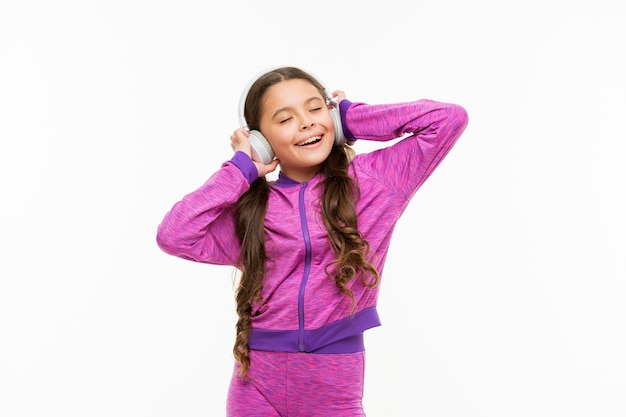 What a great feeling Athletic little girl relaxing isolated on white Cute girl child listening to music Fit small girl wearing headphones Active girl enjoy music playing in earphones