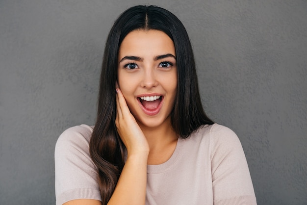 What a great surprise! Excited young woman touching face and keeping mouth open