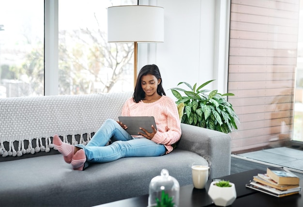 What I prefer to do on the weekend Cropped shot of a beautiful young woman using a tablet while chilling on the sofa in the living room at home