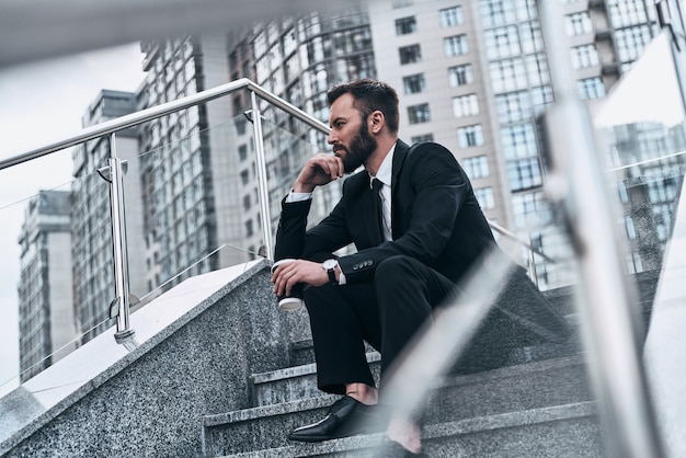 What if... Good looking young man in full suit holding disposable cup and looking away