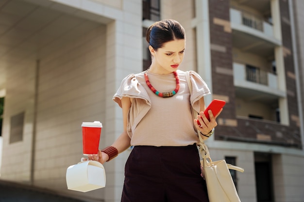 What is this. Nice young woman looking at her smartphone screen while receiving a message from the office