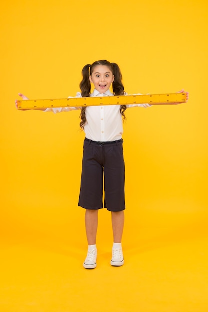 What a long ruler Surprised little student holding rigid wooden ruler on yellow background Small child taking measurements with metric ruler My ruler is one meter long