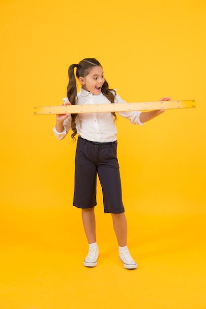 What a reason for sirprise Surprised pupil or young learner Cute pupil holding long ruler on yellow background Small pupil getting ready for math and geometry lesson Little pupil back to school