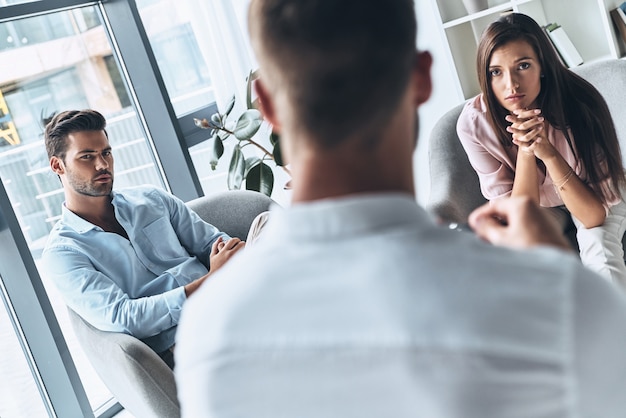 What should we do? Young married couple looking at psychologist while sitting on the therapy session