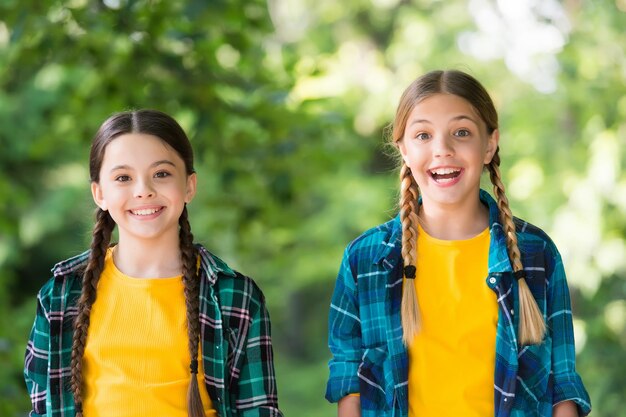 Photo what a surprise little kids girls in shirt two young smiling hipster girls in trendy summer clothes carefree kids posing outdoor positive models casual hipsters outfit portrait of happy sisters