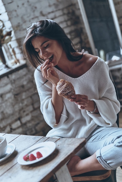 なんておいしい朝食でしょう。目を閉じてクロワッサンを保持している魅力的な若い女性