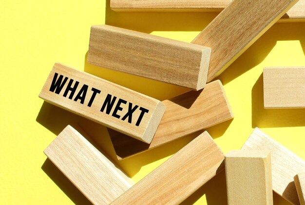 The WHAT NEXT text is written on one of the many scattered wooden blocks against a yellow background