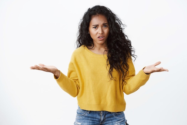 What wrong with you Confused and intense pissed africanamerican woman in yellow sweater shrugging spread hands sideways in dismay complaining friend being late white background Copy space