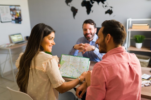 What do you think of this traveling destination? Beautiful young girlfriend holding a map and asking her boyfriend where to go on vacation at the travel office