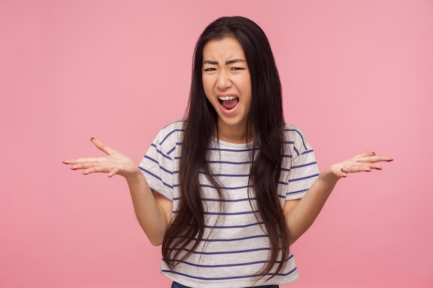 What do you want, portrait of enraged irritated girl with\
brunette hair raising hands in questioning gesture, scolding and\
screaming, having conflict. indoor studio shot isolated on pink\
background