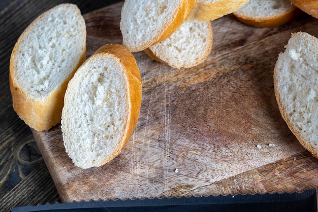 Пшеничный багет, нарезанный кусочками на разделочной доске