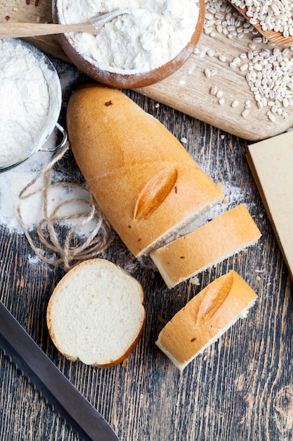 A wheat baguette on the table with flour and various plant grains a kitchen table with bread and ingredients for it porridge and rice