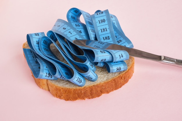 Wheat bread slice, butter knife and blue measuring tape on pink