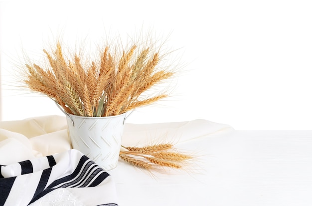 Wheat ears in a bucket, tallit on a wooden table