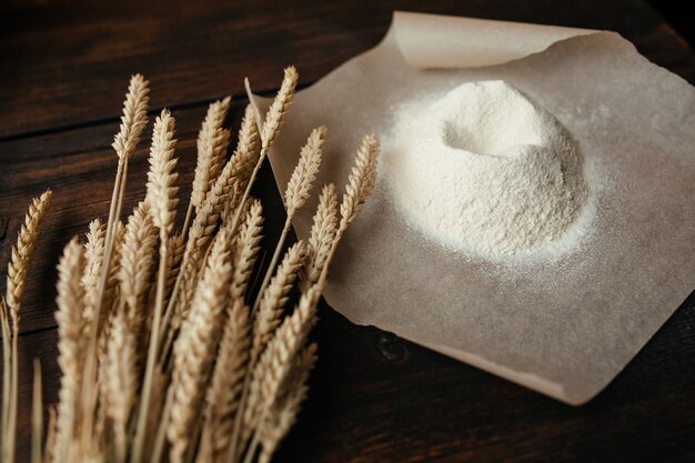 Photo wheat ears and flour on tracing paper on a dark wooden background