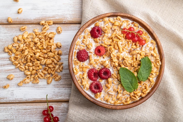 Wheat flakes porridge with milk raspberry and currant in wooden bowl on white wooden background Top view flat lay close up