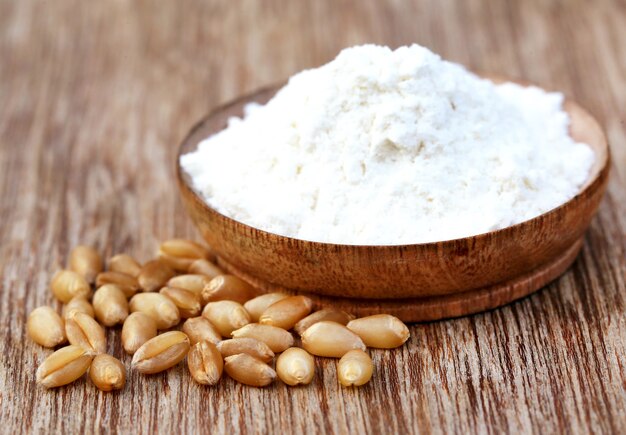 Wheat and flour on a bowl on wooden surface